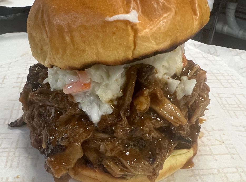 Mouth-watering close-up of a pulled pork sandwich with fresh ingredients and sesame seed bun.
