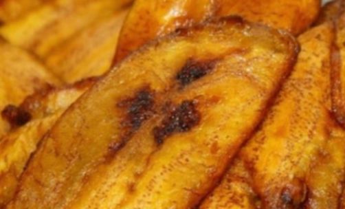 A vibrant African meal featuring fried plantains, chicken, and corn on a wooden table.