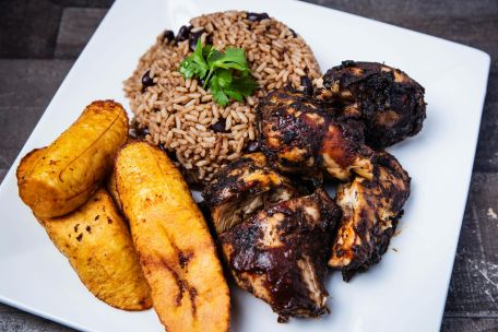 Tantalizing Caribbean jerk chicken served with rice and beans and fried plantains on a square plate.