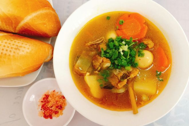 A hearty Vietnamese soup served with fresh baguette and condiments, perfect for lunch.