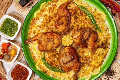 Savory roasted chicken on a bed of rice with lentils, accented by spicy and fresh green sides.