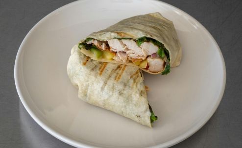 Close-up of a tasty grilled chicken wrap with fresh ingredients on a plate.
