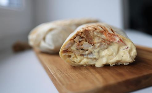 Tasty chicken wrap filled with creamy sauce on a wooden cutting board.