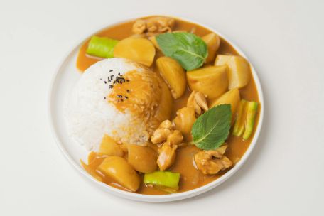 From above of appetizing dish of Indian cuisine curry made of vegetables and meat and served with rice and green leaves