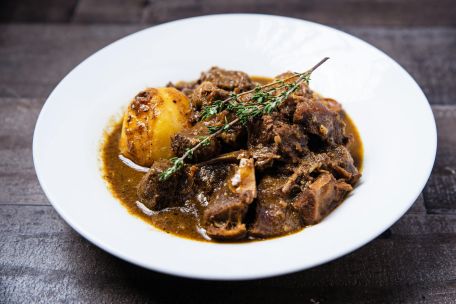 Close-up of savory Caribbean oxtail stew with potatoes served on a white plate.