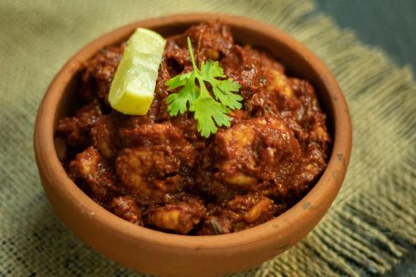 Close-up of a spicy Indian dish in a clay bowl garnished with lime and cilantro.