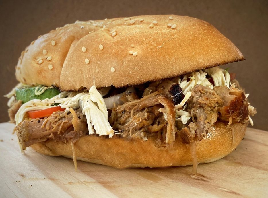 Mouth-watering close-up of a pulled pork sandwich with fresh ingredients and sesame seed bun.