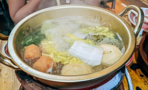 Steaming hot pot filled with fresh vegetables and meatballs, prepared on a stove.