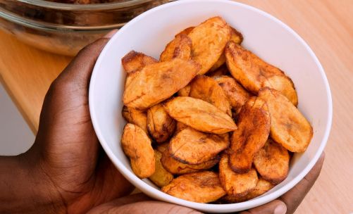 A vibrant African meal featuring fried plantains, chicken, and corn on a wooden table.