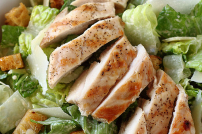 Delicious chicken salad with spinach, feta cheese, and creamy sauce on a white plate.