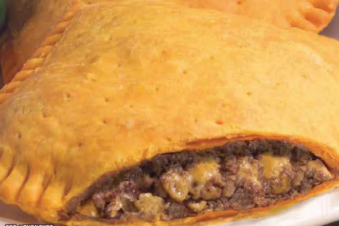 Baked empanadas in a dish with fresh vegetables on a vibrant table.